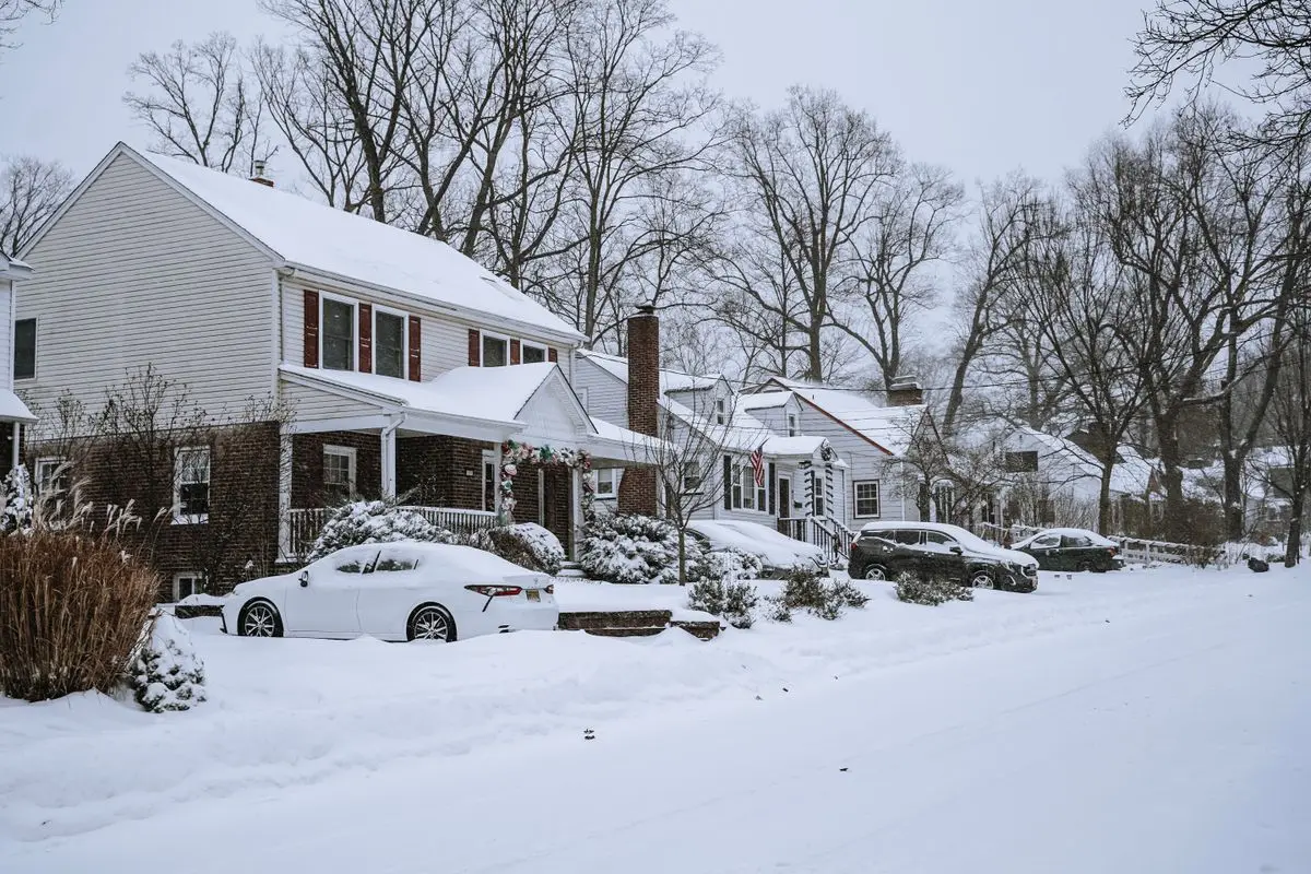 Suburban street under snow with houses and parked cars